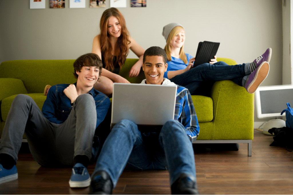 Group of teens hanging out, one on a laptop and one on a tablet